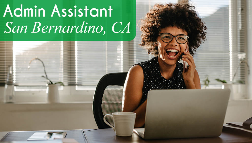 Image shows a woman sitting at a desk, smiling and talking on the phone. Now hiring an Administrative Assistant in San Bernardino, CA