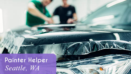 Image shows a closeup of a vehicle taped off for painting, with two people painting in the background. Now Hiring a Painter Helper in Seattle, WA. All StarZ Staffing.