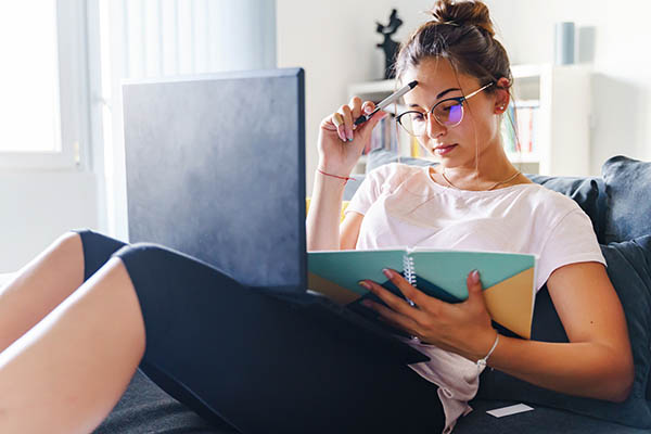 Image shows a woman on a couch with a laptop and a notebook. Find out how to use AI to optimize your cover letter.