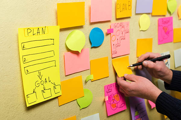 Image shows post it notes on a wall with brainstorming notes and hands writing on them. All StarZ Staffing.