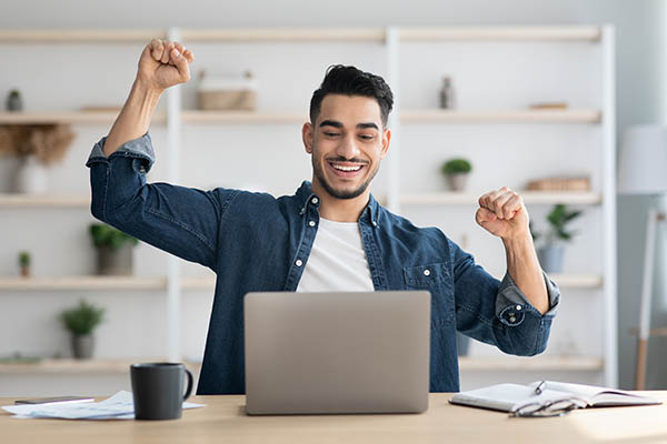 Image shows a man celebrating finishing his resume with a laptop and coffee mug.