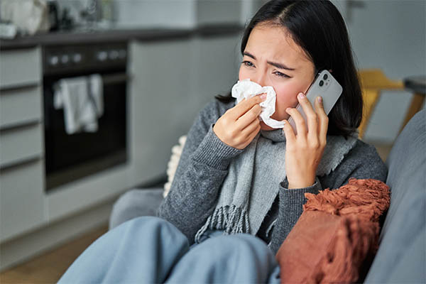 Image shows a woman with a Kleenex talking on the phone, calling out sick.