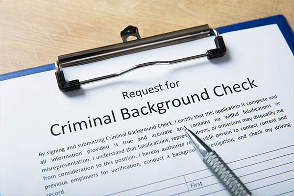 Image shows the top of a background check consent form on a blue clipboard with a pen.
