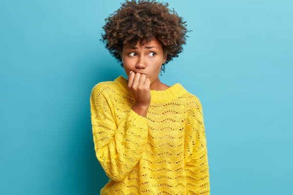 Image shows a woman with a worried expression wearing a yellow sweater in front of a blue background